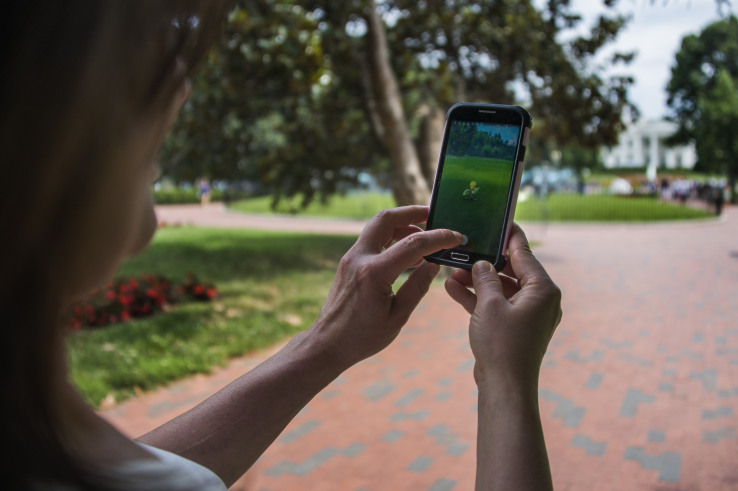 A woman holds up her cell phone as she plays the Pokemon Go game in Lafayette Park in front of the White House in Washington, DC, July 12, 2016. Pokémon Go mania is sweeping the US as players armed with smartphones hunt streets, parks, rivers and elsewhere to capture monsters and gather supplies in the hit game. The free application based on a Nintendo title that debuted 20 years ago has been adapted to the mobile internet Age by Niantic Labs, a company spun out of Google last year after breaking ground with an "Ingress" game that merged mapping capabilities with play. As of July 11, 2016 Pokémon Go had been downloaded millions of times, jumping topping rankings at official online shops for applications tailored for smartphones powered by Apple or Google-backed Android software. / AFP / JIM WATSON (Photo credit should read JIM WATSON/AFP/Getty Images)