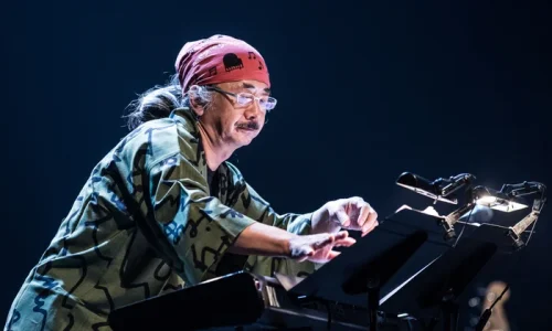 Nobuo Uematsu si esibisce dal vivo al pianoforte durante un concerto, illuminato dalle luci del palco.