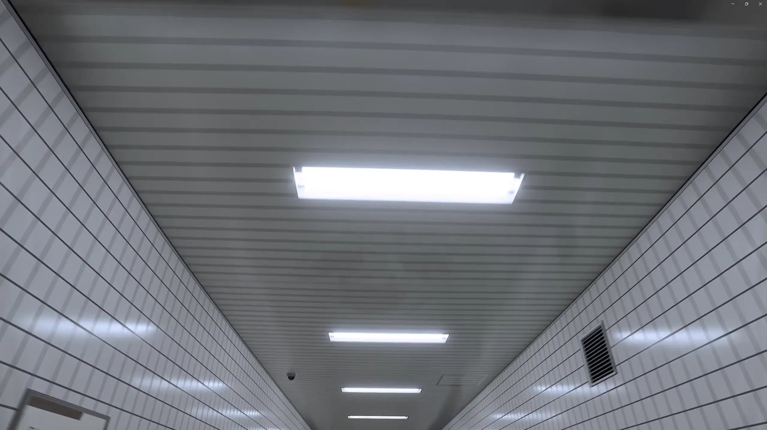 Soffitto di un corridoio piastrellato illuminato da luci al neon allineate.